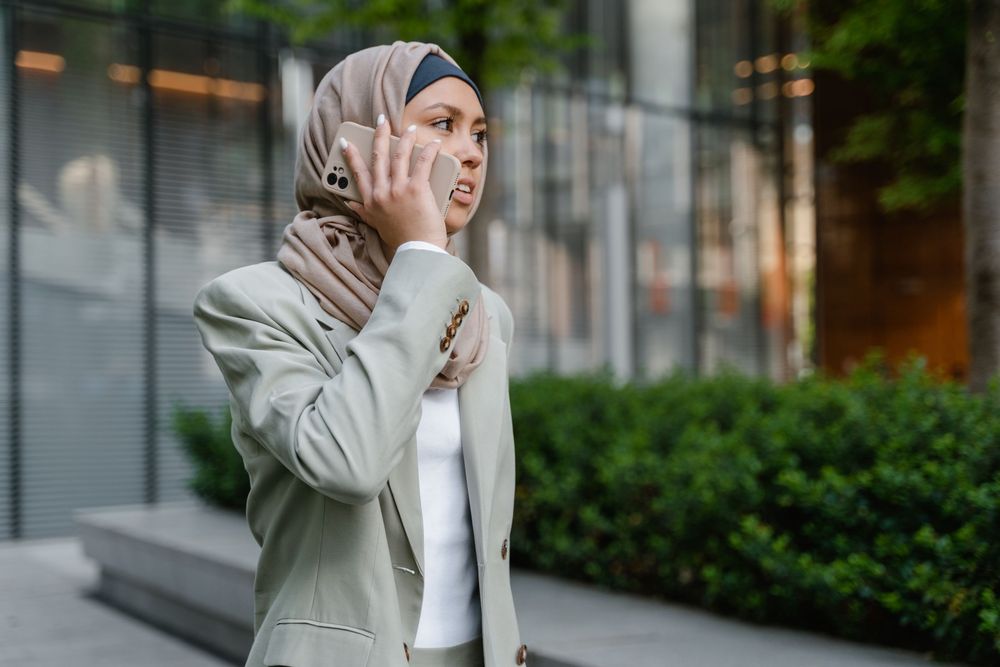 A consultant in a hijab taking a call outside a glass office building